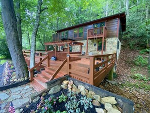 Une cabane dotée d’une terrasse en bois, de murs en pierre et d’un chemin en pierre menant à l’entrée.