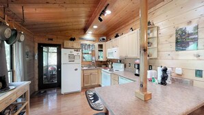 Une cuisine rustique aménagée dans une cabane en bois, avec un réfrigérateur, une cuisinière et des placards en bois.