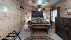 Een slaapkamer in een houten blokhut met een bed, een dressoir en een plafondventilator.