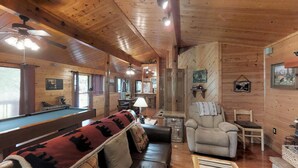 Un intérieur de chalet chaleureux avec une table de billard, un canapé, un fauteuil inclinable et un coin repas.