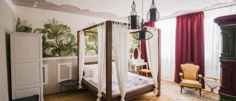 A four-poster bed with a canopy, a desk with a chair, a red curtain, and a plant wall.