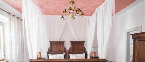 A room with a pink ceiling, white drapes, a chandelier, wooden furniture, and a radiator.