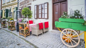 Una calle adoquinada con un restaurante llamado "Kromlovska Pohadka" que ofrece terraza con mobiliario de mimbre y cojines rojos.