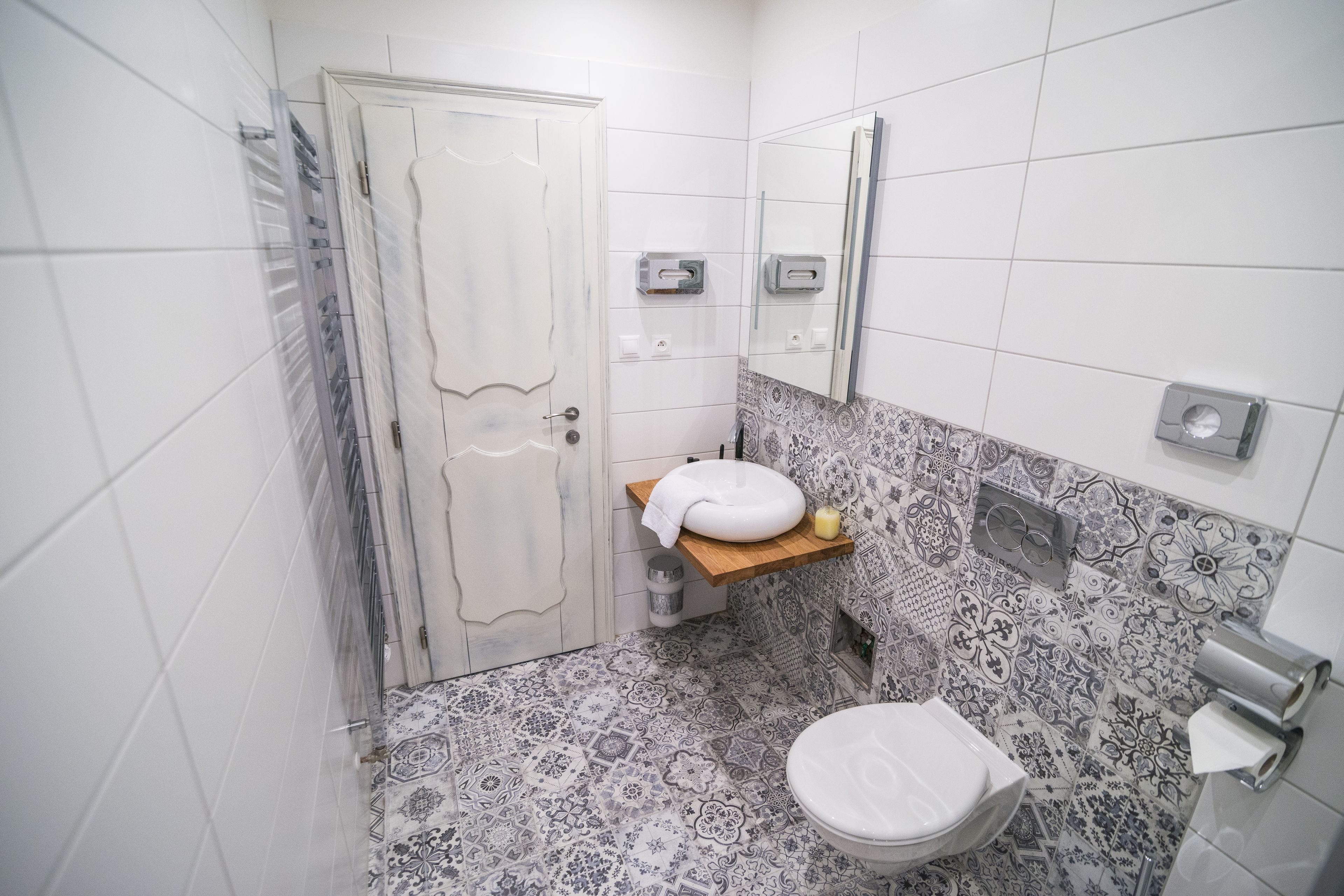 A bathroom with a white door, a sink with a towel, a toilet, and patterned tiles.