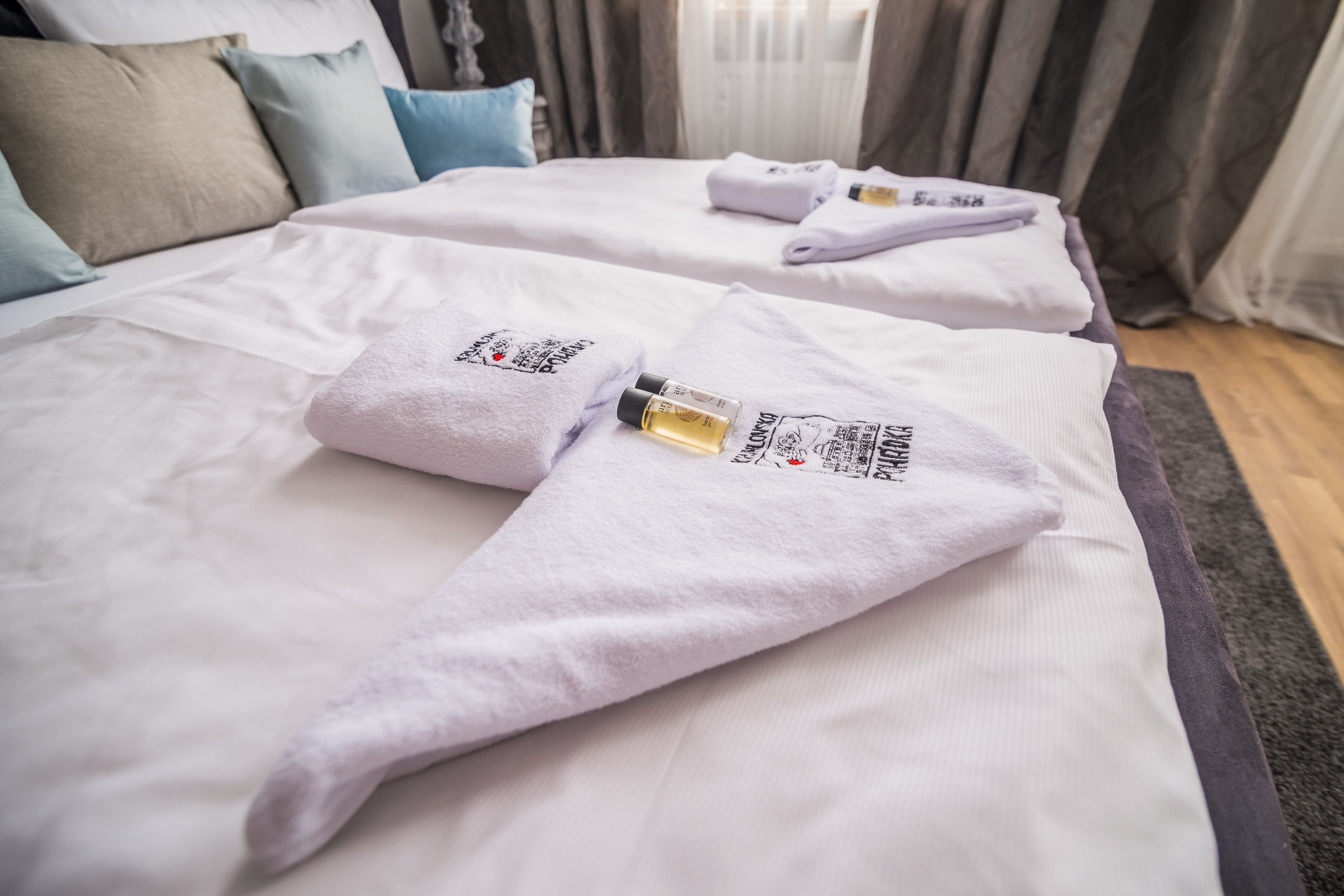 A hotel room with two beds, each with a towel and a bottle of lotion.