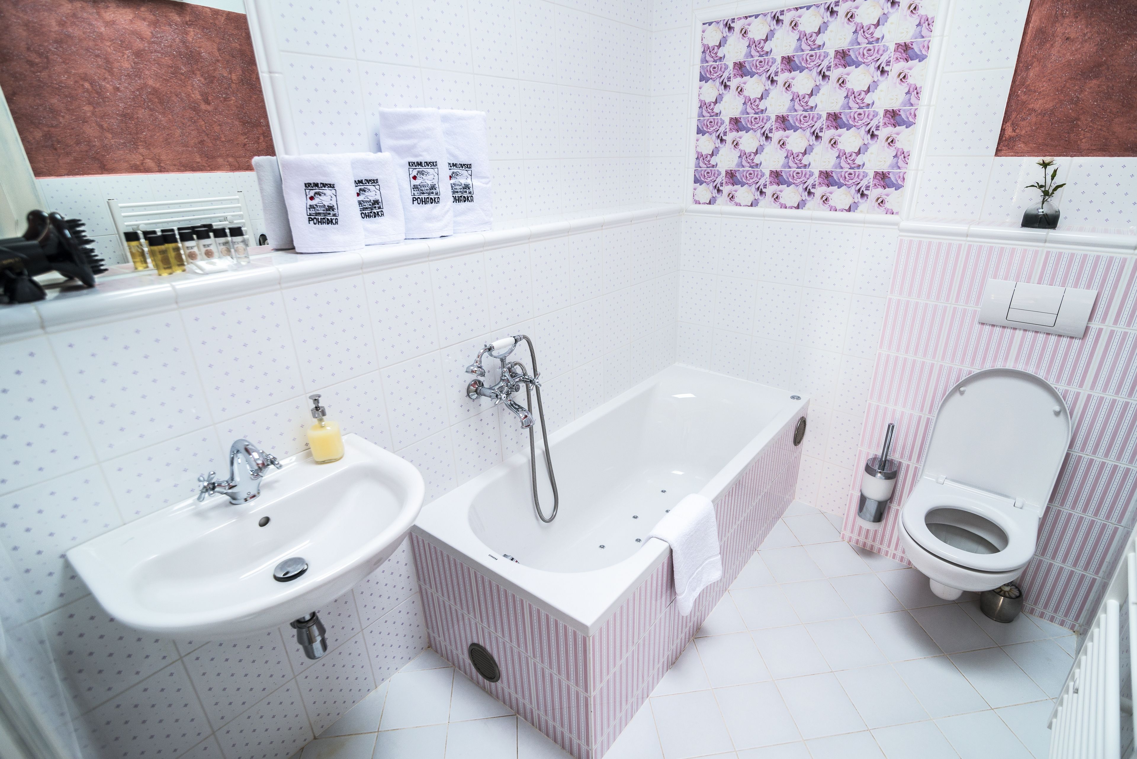 A bathroom with a sink, bathtub, and toilet. There are toiletries on the counter and a showerhead above the bathtub.