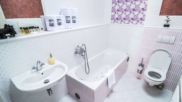 Baño con lavamanos, bañera e inodoro. Hay artículos de aseo en la encimera y una ducha sobre la bañera.