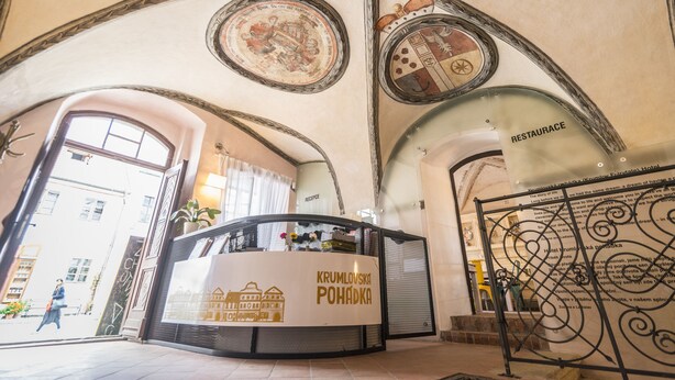 Zona de recepción con un mostrador identificado como "KRUMLOVSKA POHADKA" y un letrero que indica "RESTAURANTE".