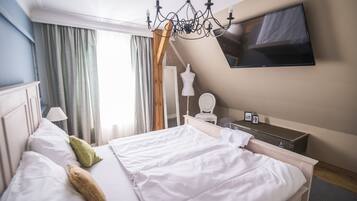 A hotel room with a large bed, a TV mounted on the wall, a dresser, and a window with curtains.