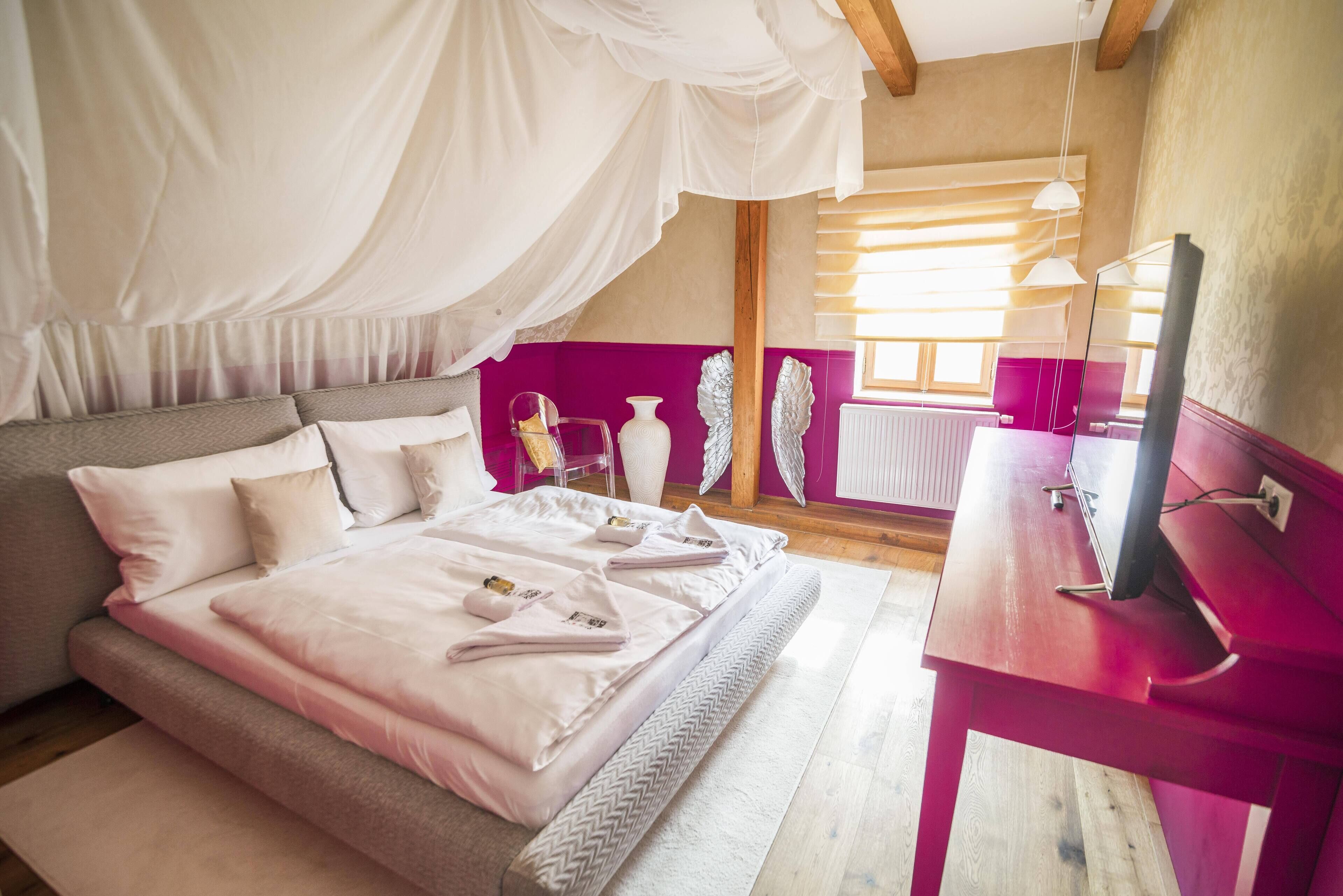 A bedroom with a bed, a desk, and a window with curtains.