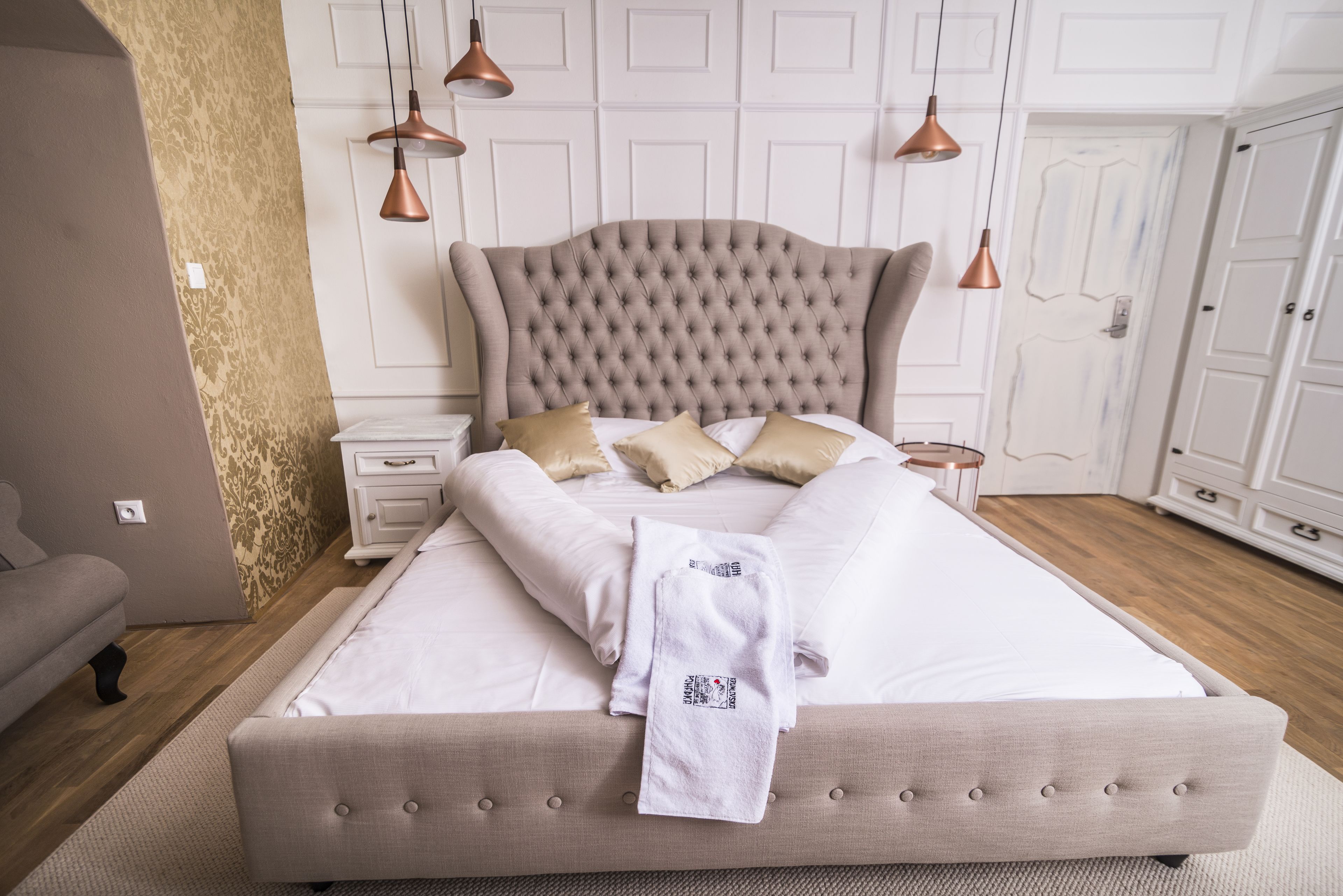 Una cama bien hecha con cabecera capitonada, un albornoz blanco sobre la cama y suelo de madera.