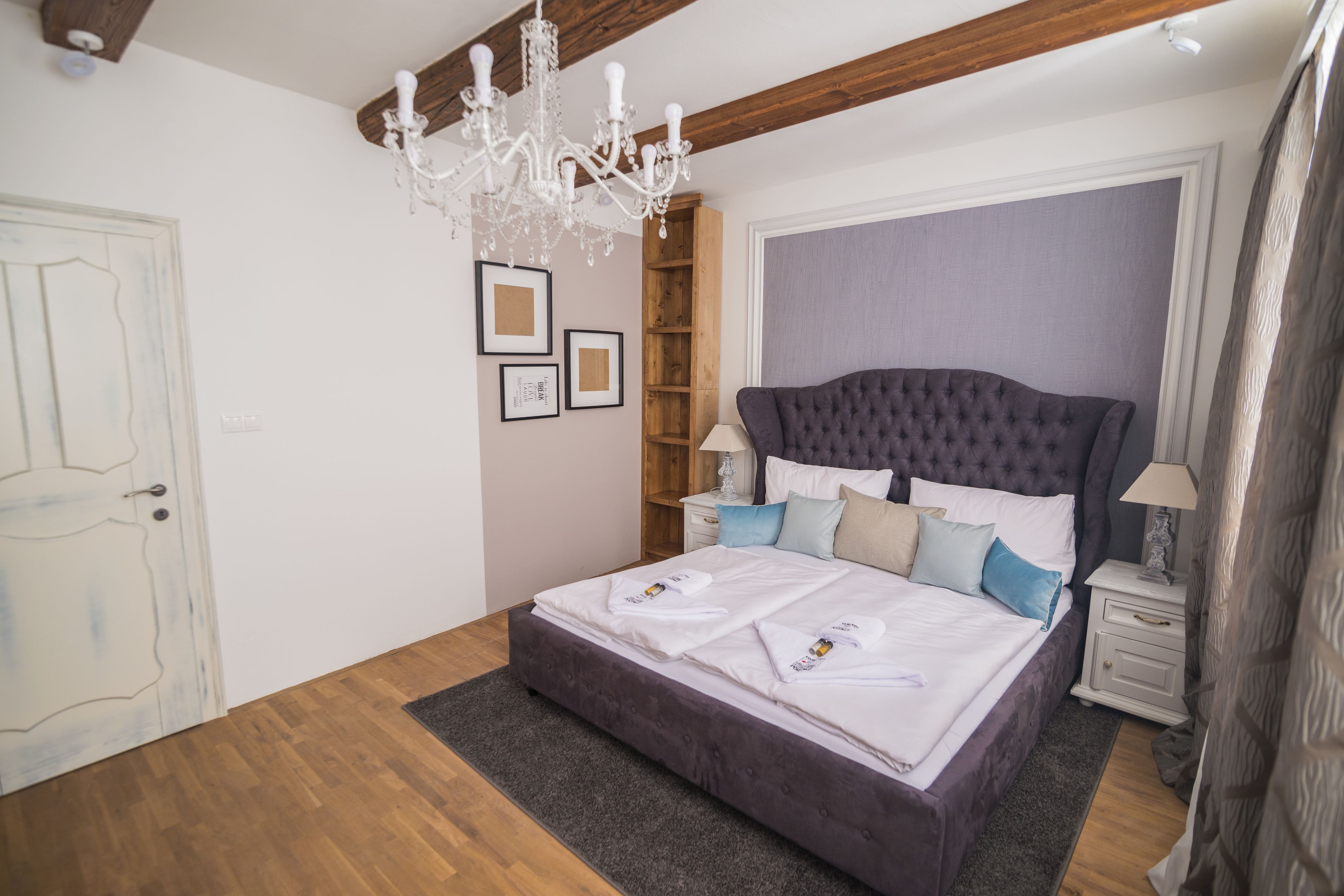 A bedroom with a large bed, wooden floor, a chandelier, a nightstand, and a wardrobe.