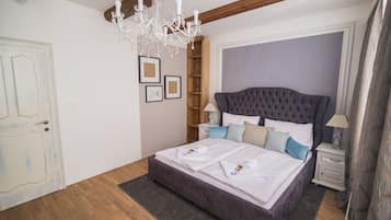 Un dormitorio con una cama grande, suelo de madera, un candelabro, una mesita de noche y un armario.