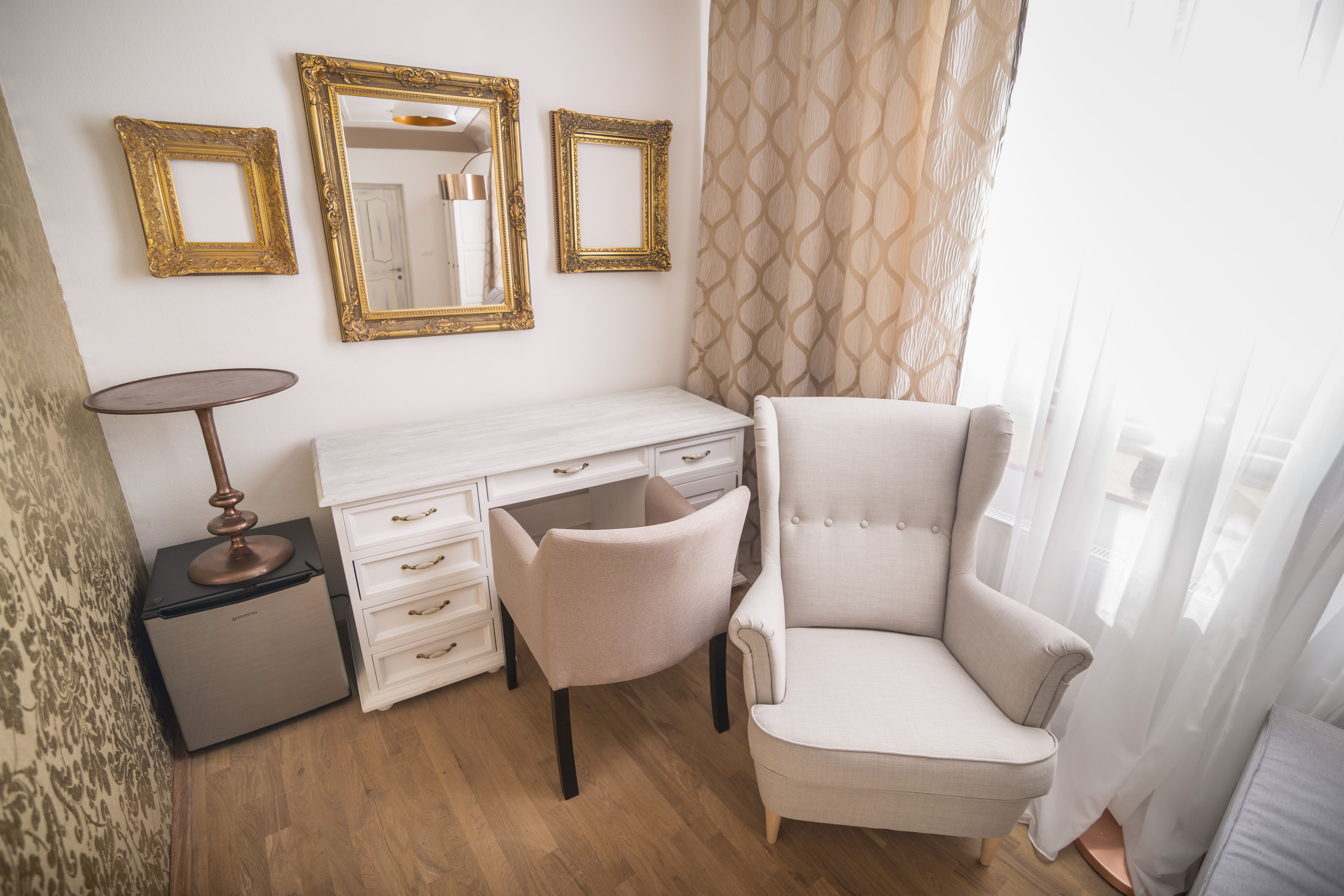 Ein Zimmer mit einem weißen Schminktisch, einem Stuhl und zwei goldgerahmten Spiegeln an der Wand.