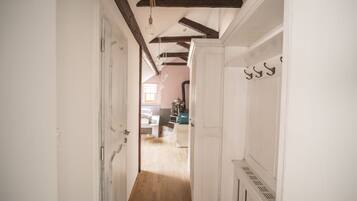 A narrow hallway with wooden beams on the ceiling, white walls, and a door on the left.