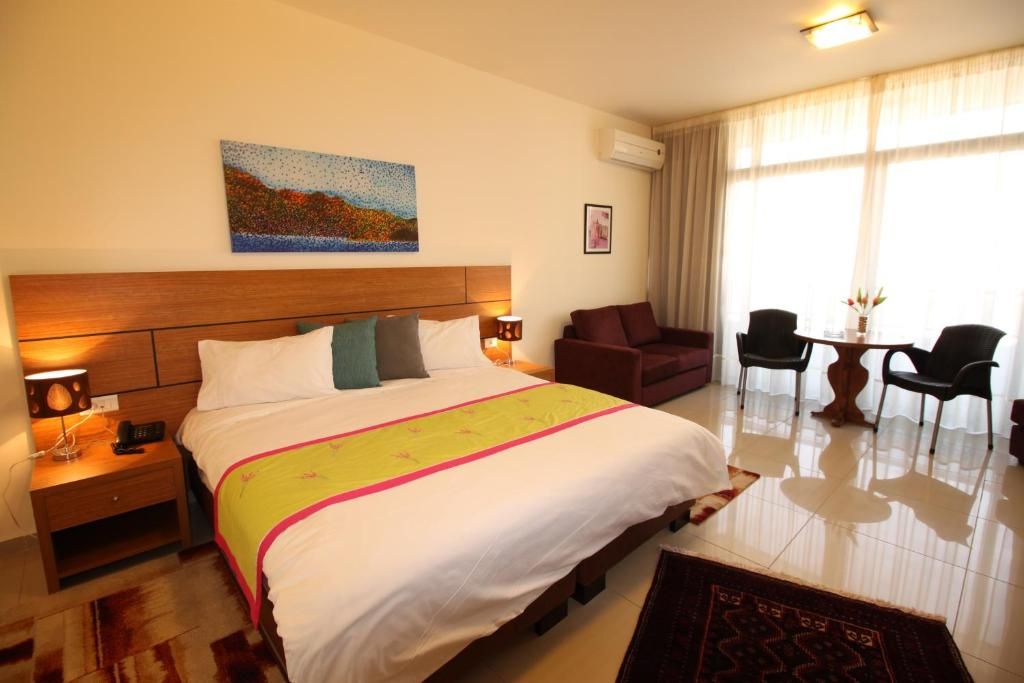A hotel room with a large bed, bedside tables, a desk with chairs, and a painting on the wall.