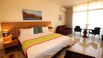 A hotel room with a large bed, bedside tables, a desk with chairs, and a painting on the wall.