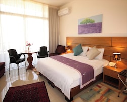 Habitación de hotel con una cama grande, una mesita de noche con lámpara, una silla, una pequeña mesa con un florero y un cuadro en la pared.