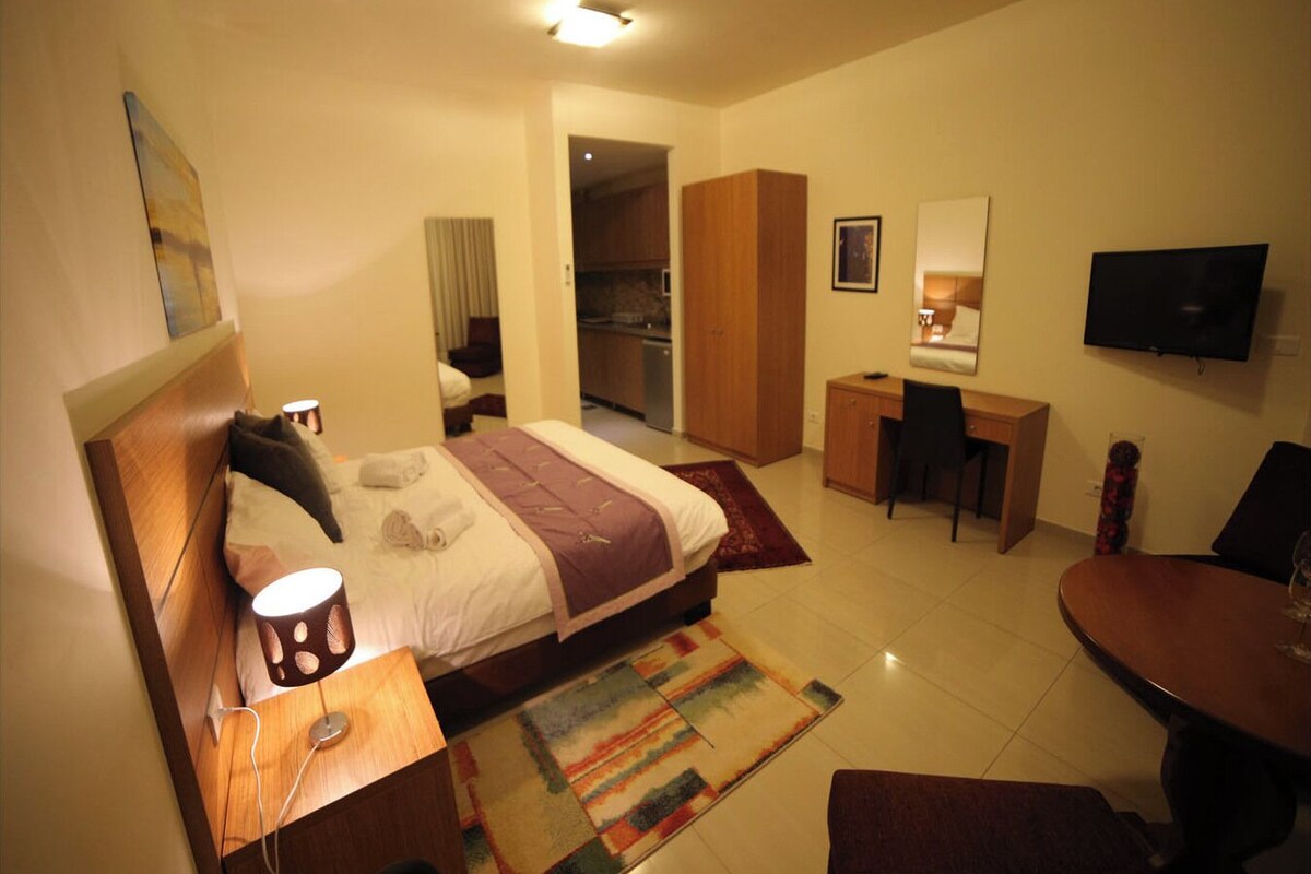 A hotel room with a bed, desk, chair, TV, and a small dining table.