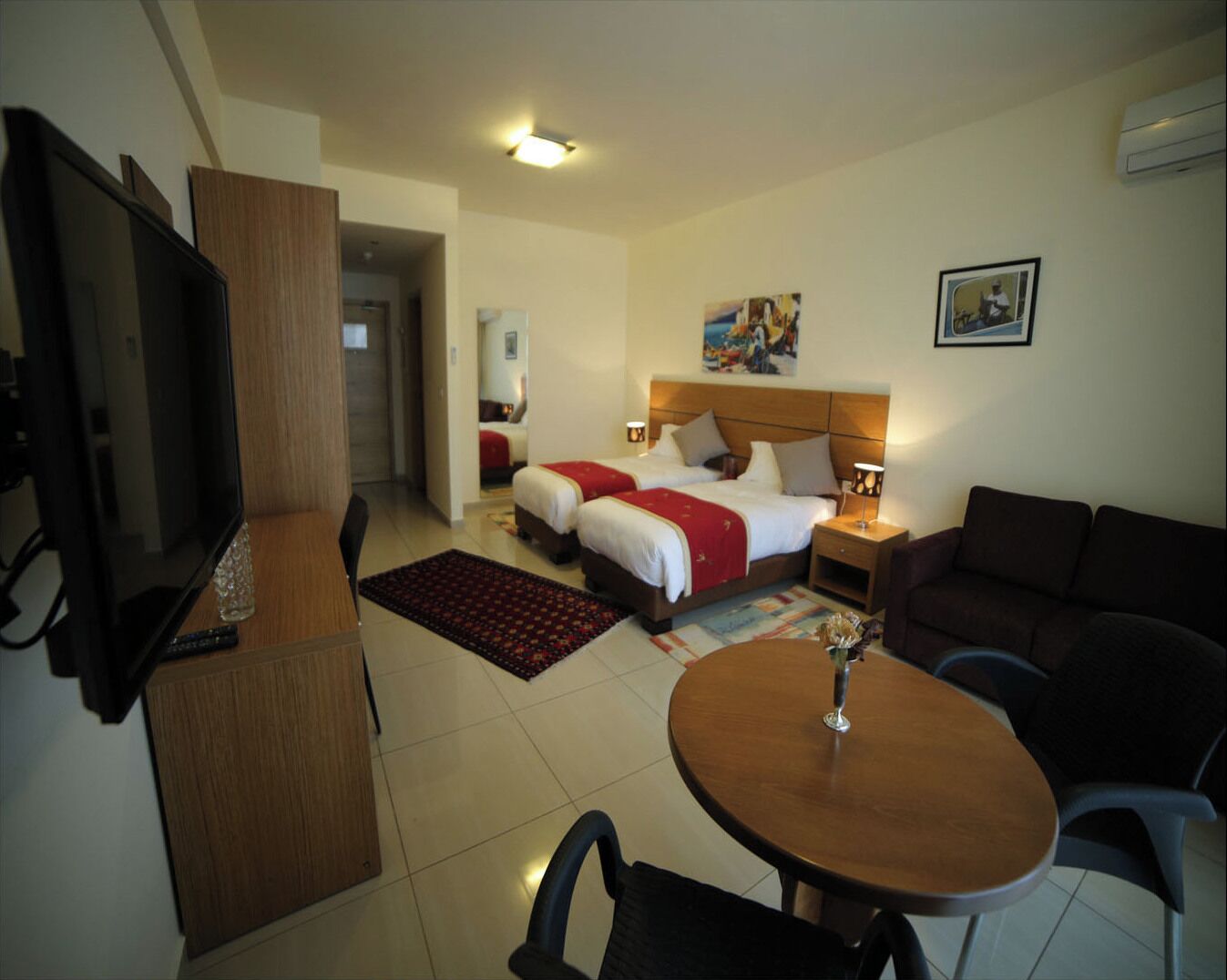 Een hotelkamer met twee bedden, een televisie, een eettafel en een bank.