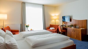A hotel room with two beds, a desk, a chair, a television, and a large window with curtains.