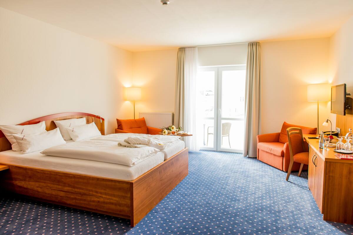 A hotel room with a wooden bed, a desk, a chair, and a view of the outside.