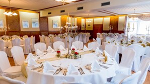 A banquet hall with round tables set for a formal event, featuring white tablecloths, silverware, and floral centerpieces.