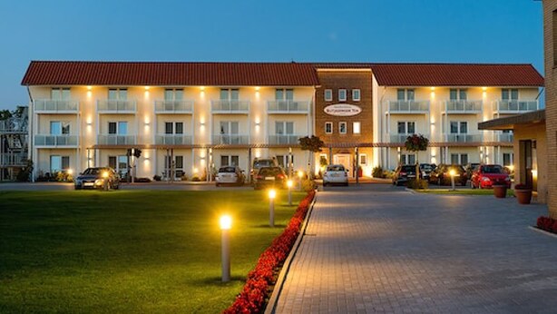 A hotel with a red roof, multiple balconies, and a paved driveway.