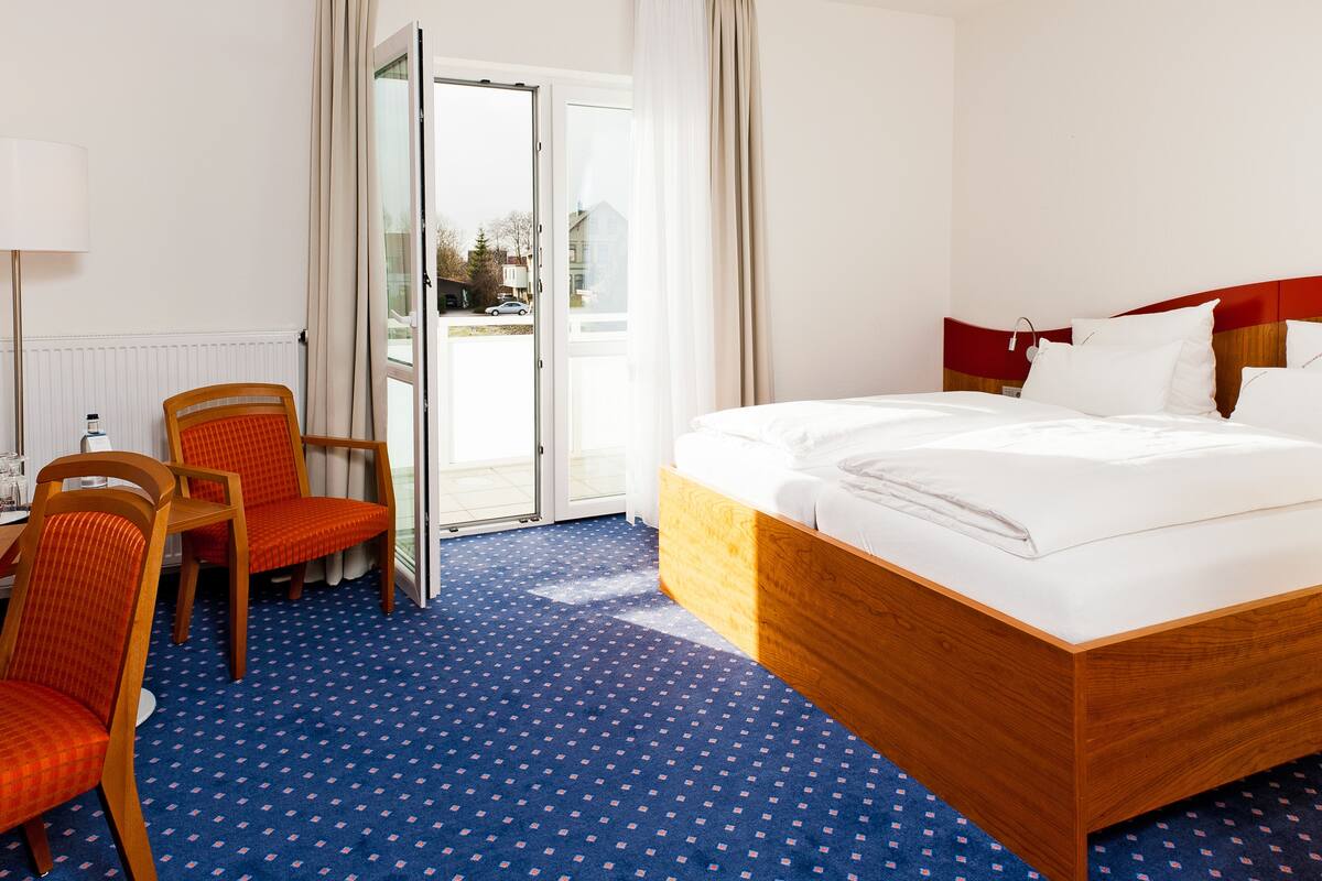 A hotel room with a bed, two chairs, a desk, and a view through a glass door.
