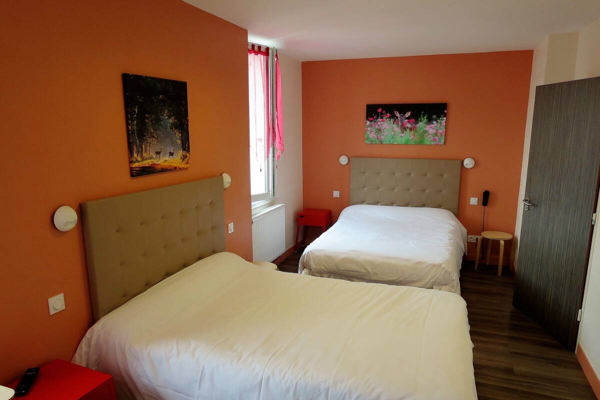 A hotel room with two beds, a red nightstand, a painting on the wall, and a window with pink curtains.