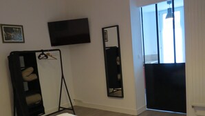 A hotel room with a bed, a TV mounted on the wall, a mirror, and a window with curtains. - Hotel Le Faisan (Saint-Avertin)