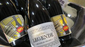 Un contenedor metálico contiene varias botellas de vino, incluyendo una botella destacada con la etiqueta 'LEGEND BEAUJOLAIS-VILLAGES 2018'.