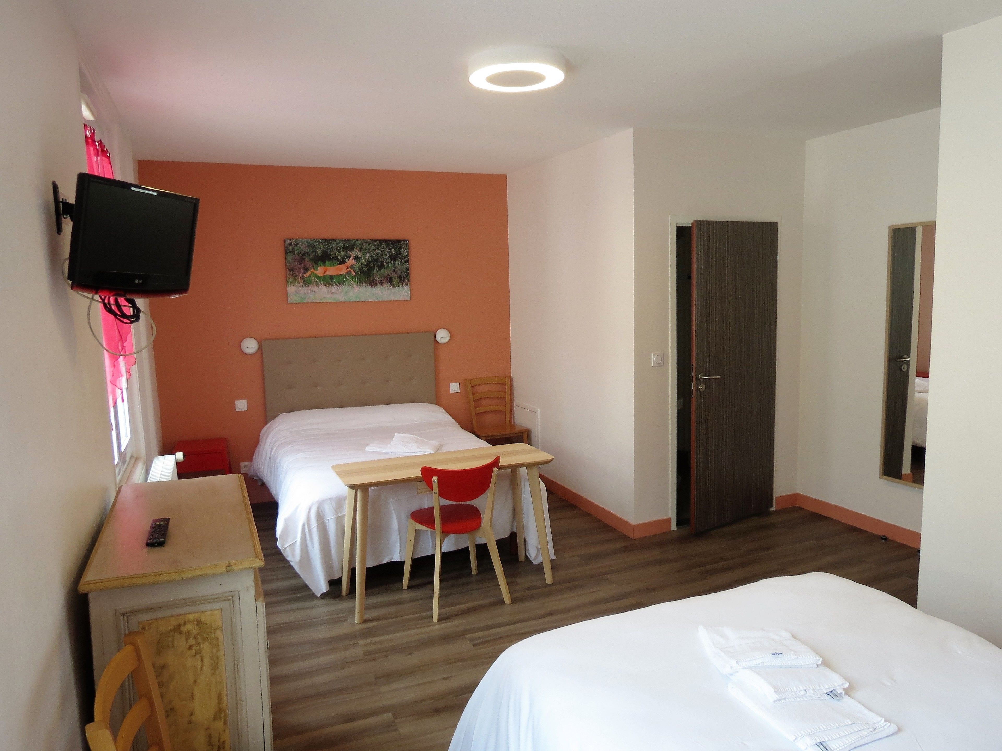 A hotel room with a bed, a desk with a chair, a television mounted on the wall, and a door.