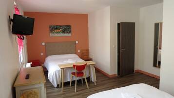 A hotel room with a bed, a desk with a chair, a television mounted on the wall, and a door.