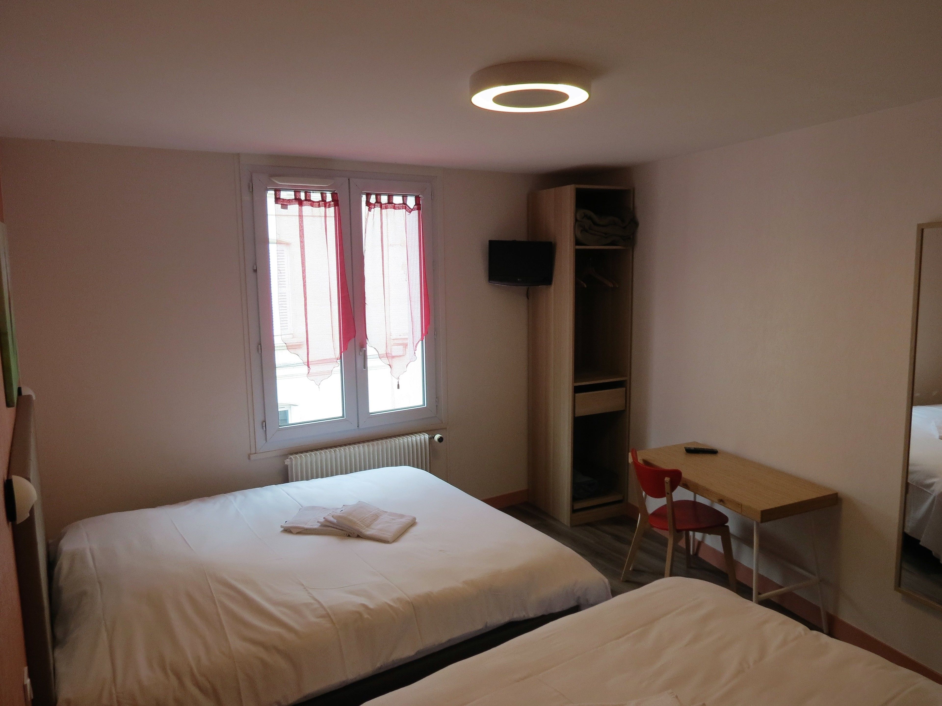 Habitación de hotel con dos camas, un escritorio, una silla, un armario y un televisor montado en la pared.