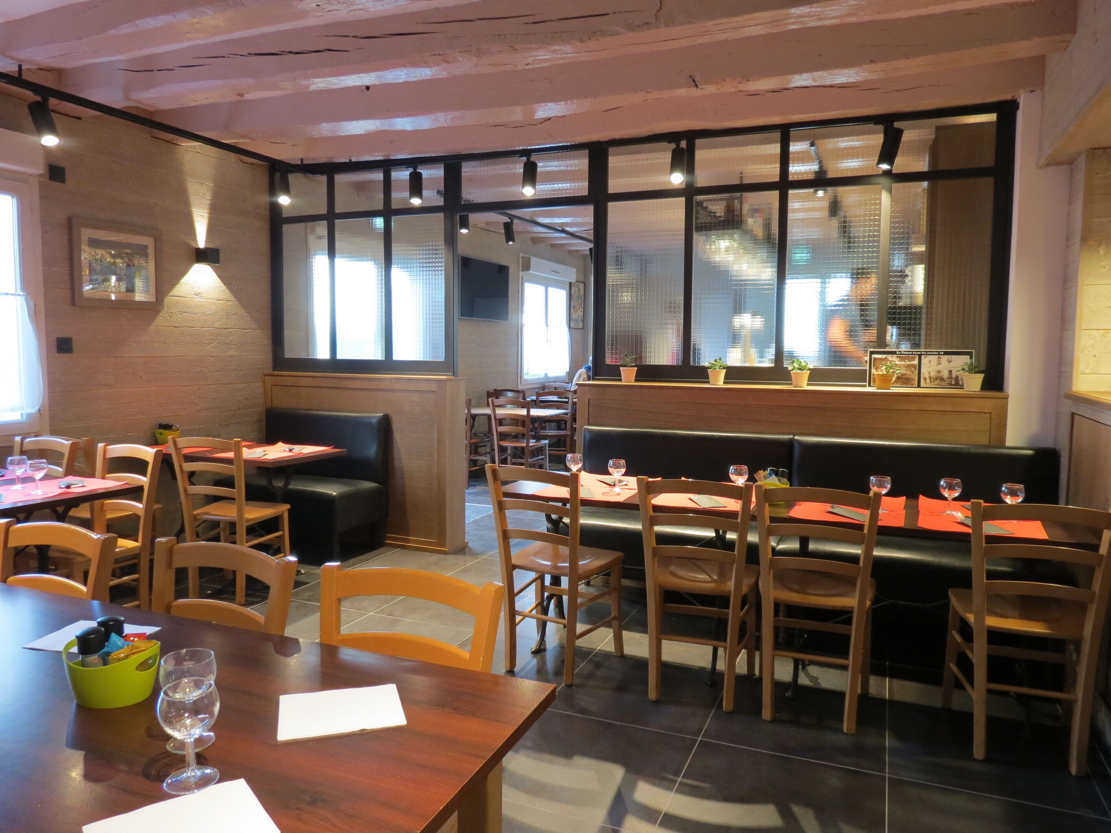 A restaurant interior with booths and tables, large windows, and potted plants on the windowsill.