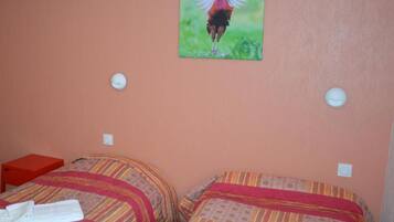 Una habitación de hotel con dos camas, cada una con una colcha estampada y una toalla blanca en una de ellas. Hay un cuadro de un pájaro en la pared.