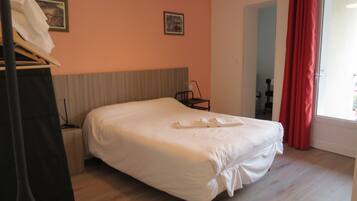 Una cama bien hecha en una habitación con suelo de madera, cabecera y ventana con cortinas rojas.