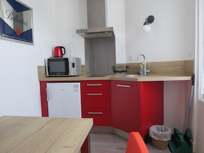 A compact kitchen with a microwave, kettle, and a small refrigerator.