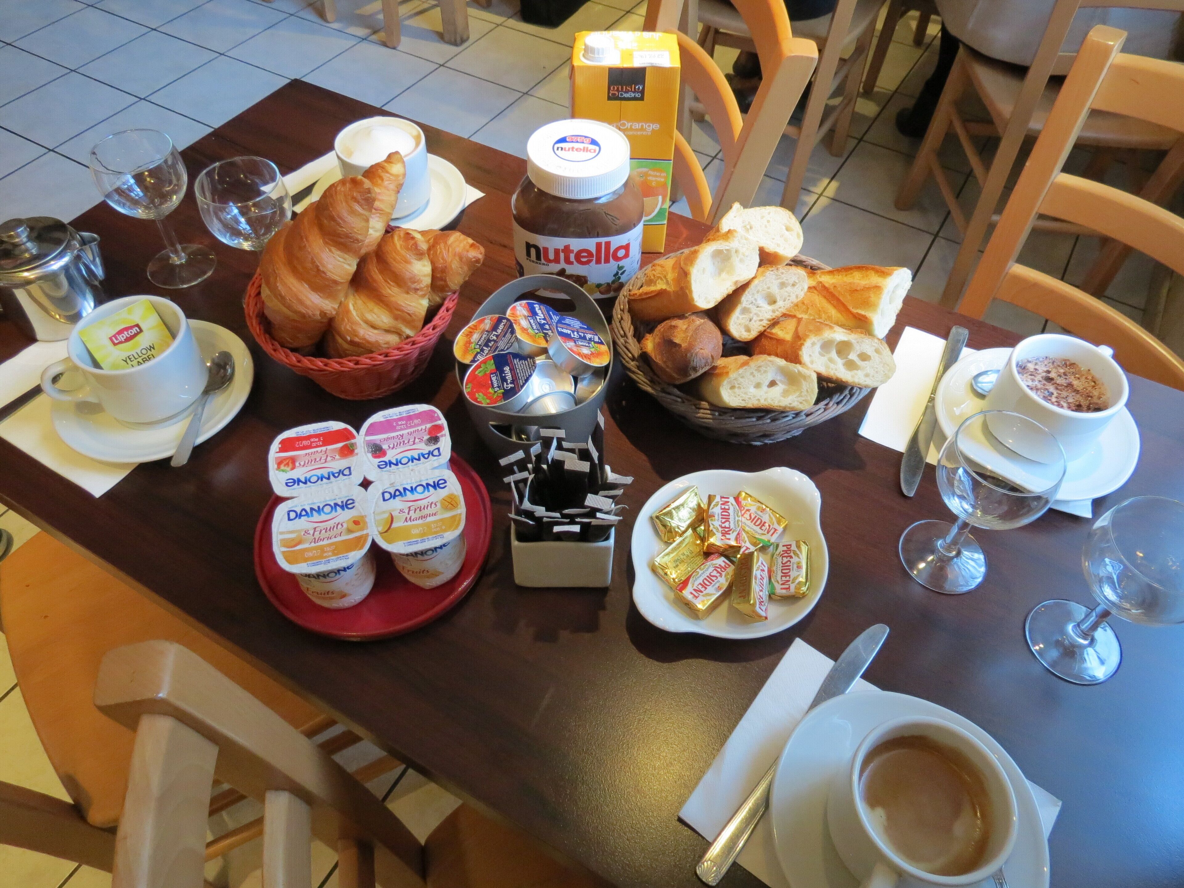 A breakfast table with croissants, Nutella, Danone yogurt, bread, and coffee.