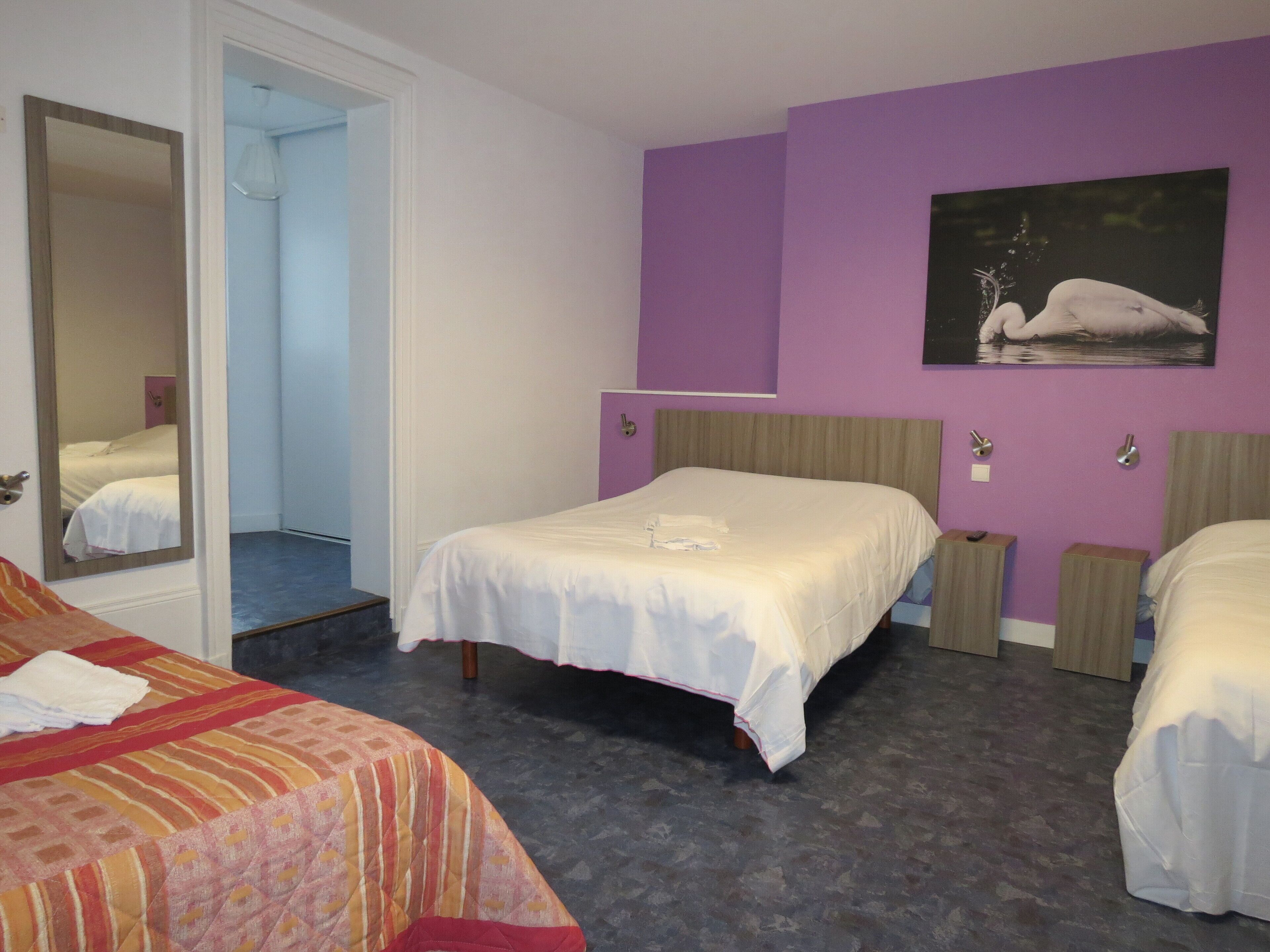 Ein Hotelzimmer mit zwei Betten, einem großen Spiegel, einem Schwandbild und einer violetten Akzentwand.