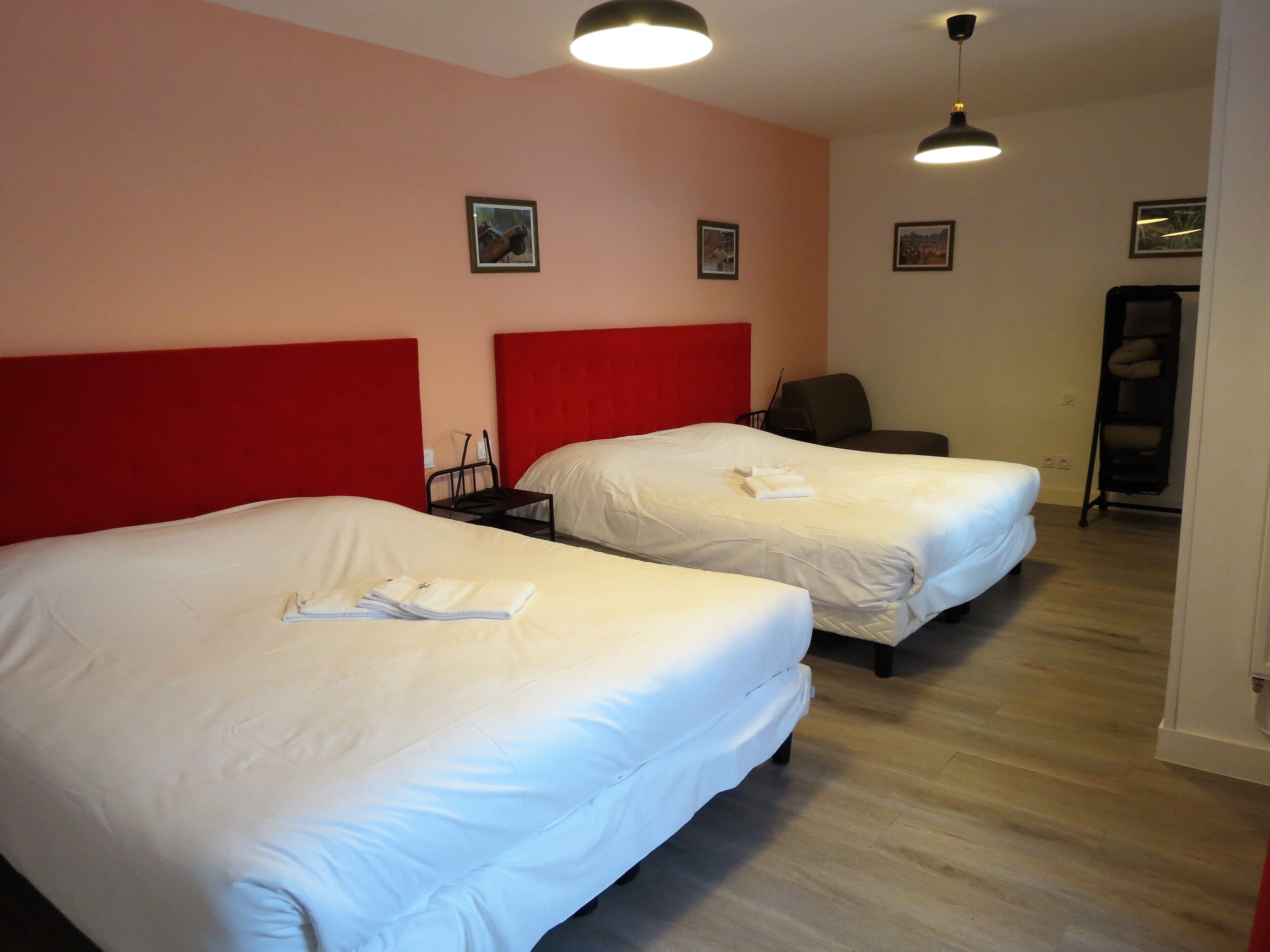 Une chambre d’hôtel avec deux lits, une tête de lit rouge et un plancher en bois.
