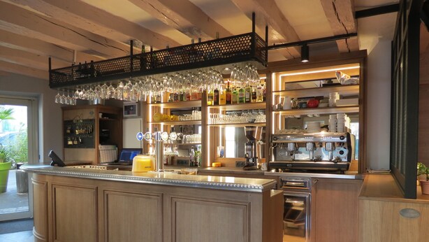 A bar area with a wooden counter, shelves with bottles and glasses, and a coffee machine. - Hotel Le Faisan (Saint-Avertin)