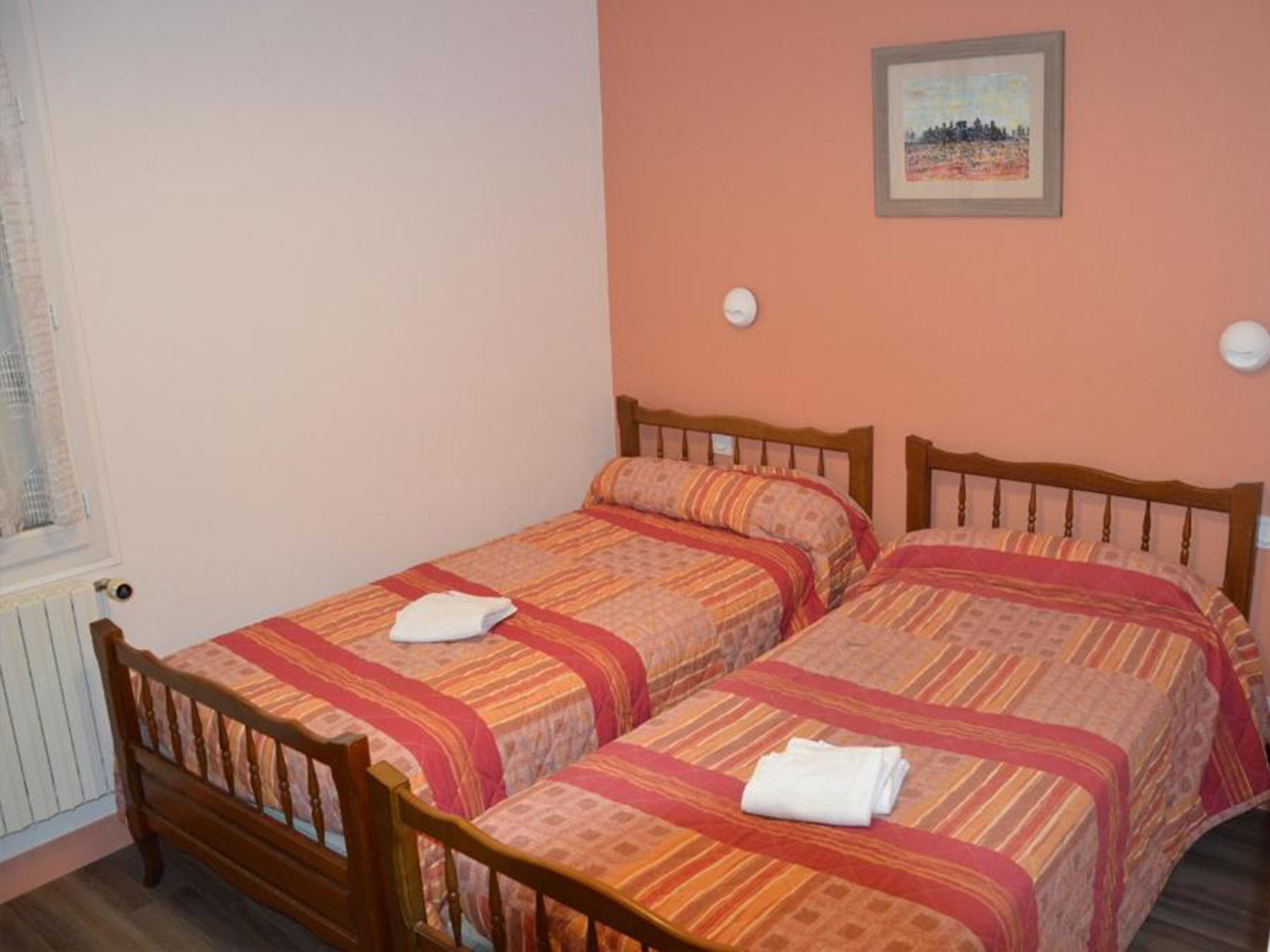 A room with two wooden beds, each with a striped bedspread and pillows. There is a framed picture on the wall above the beds.