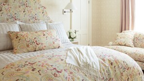 A bedroom with a floral-patterned bedspread, matching pillows, and a bedside table with a lamp and flowers.