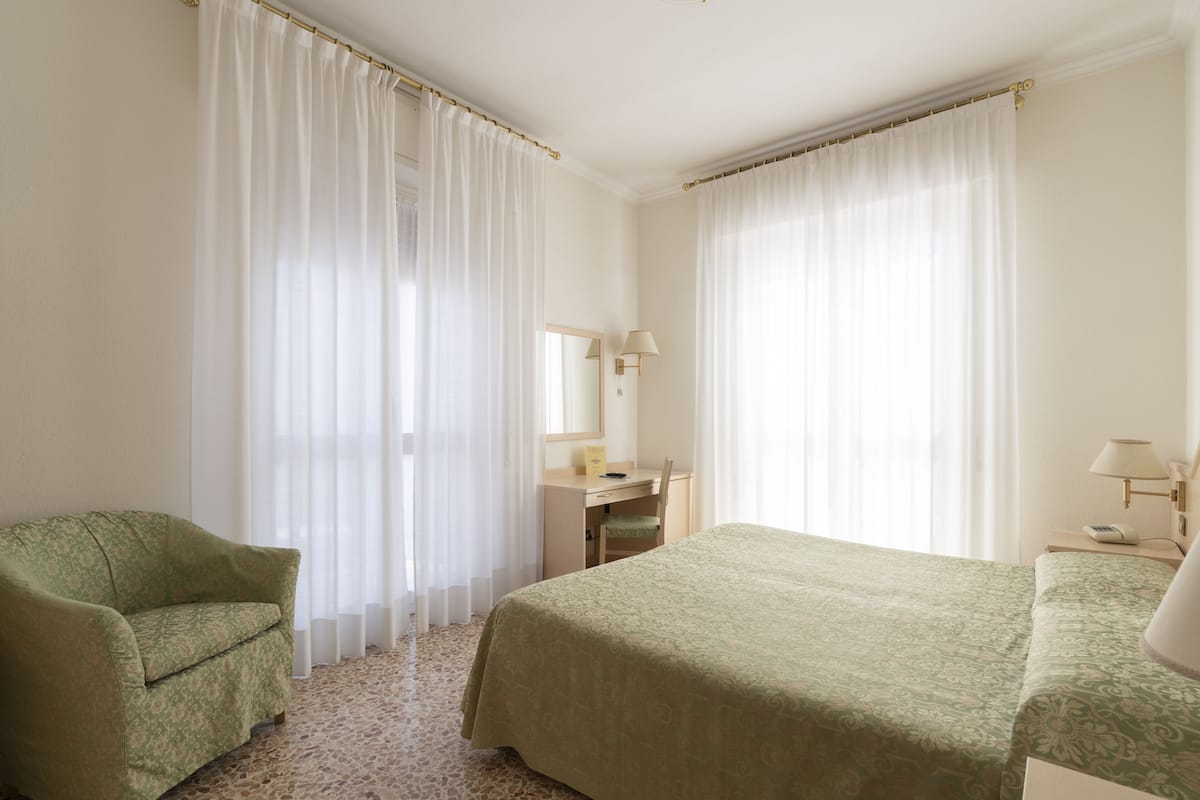 A hotel room with a bed, a desk, a chair, and a large window with curtains.