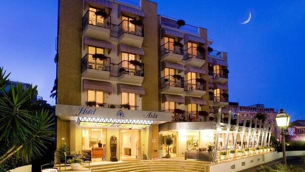 A multi-story hotel with balconies, a well-lit entrance, and a crescent moon in the sky. - Hotel Aida (Alassio)