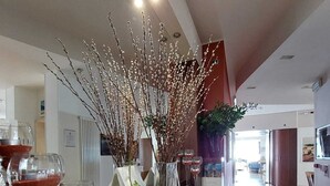 A modern interior with a wooden reception desk, clear glass wine glasses, and decorative branches. - Hotel Aida (Alassio)