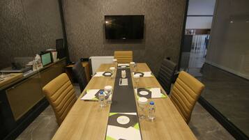 A conference room with a long table, chairs, a TV mounted on the wall, and a glass partition.