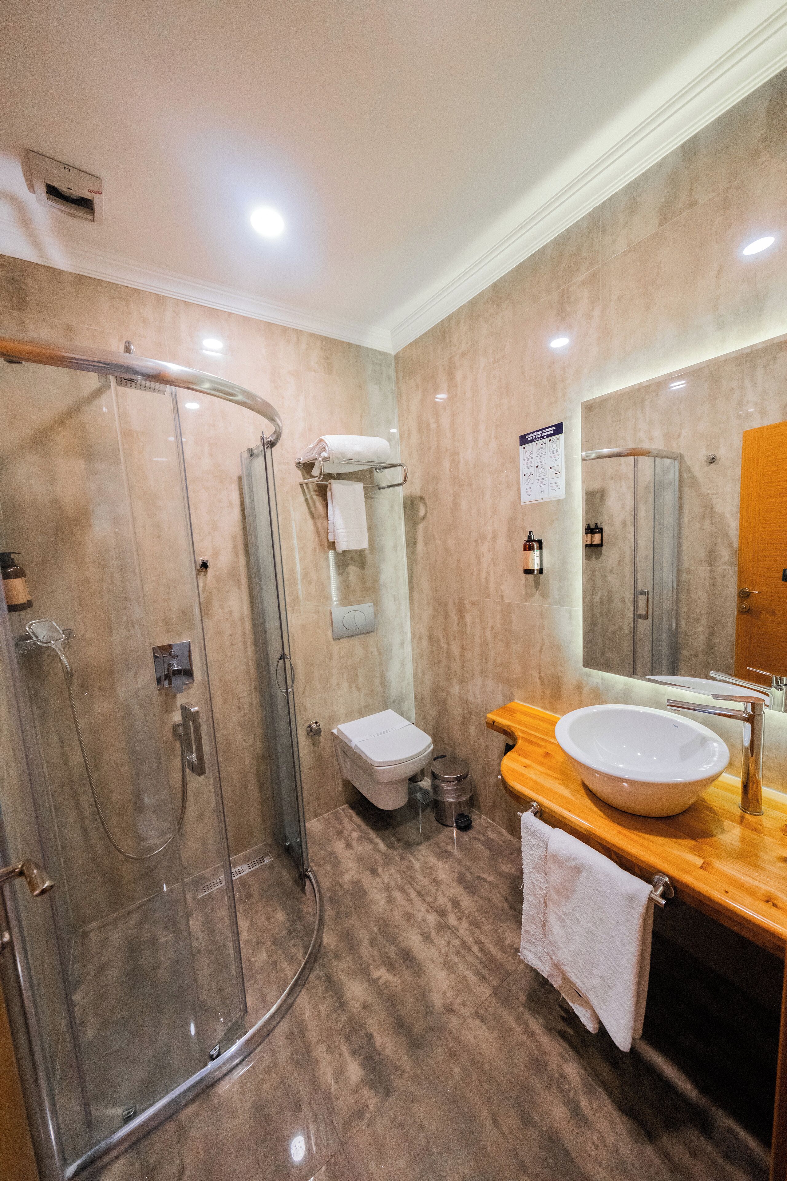 A modern bathroom with a glass-enclosed shower, a wooden vanity with a large sink, and a mirror above the sink.